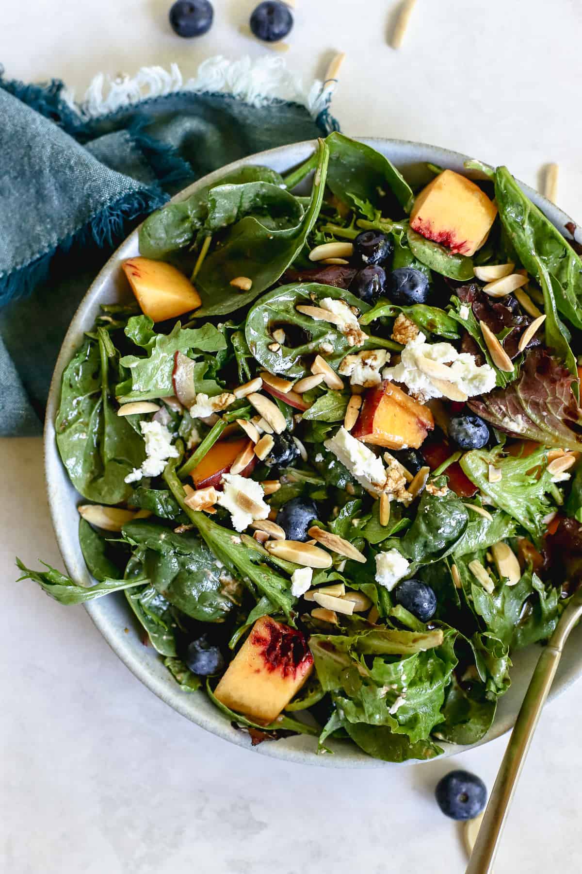 Peach blueberry salad in light blue bowl with teal linen on gray and white surface