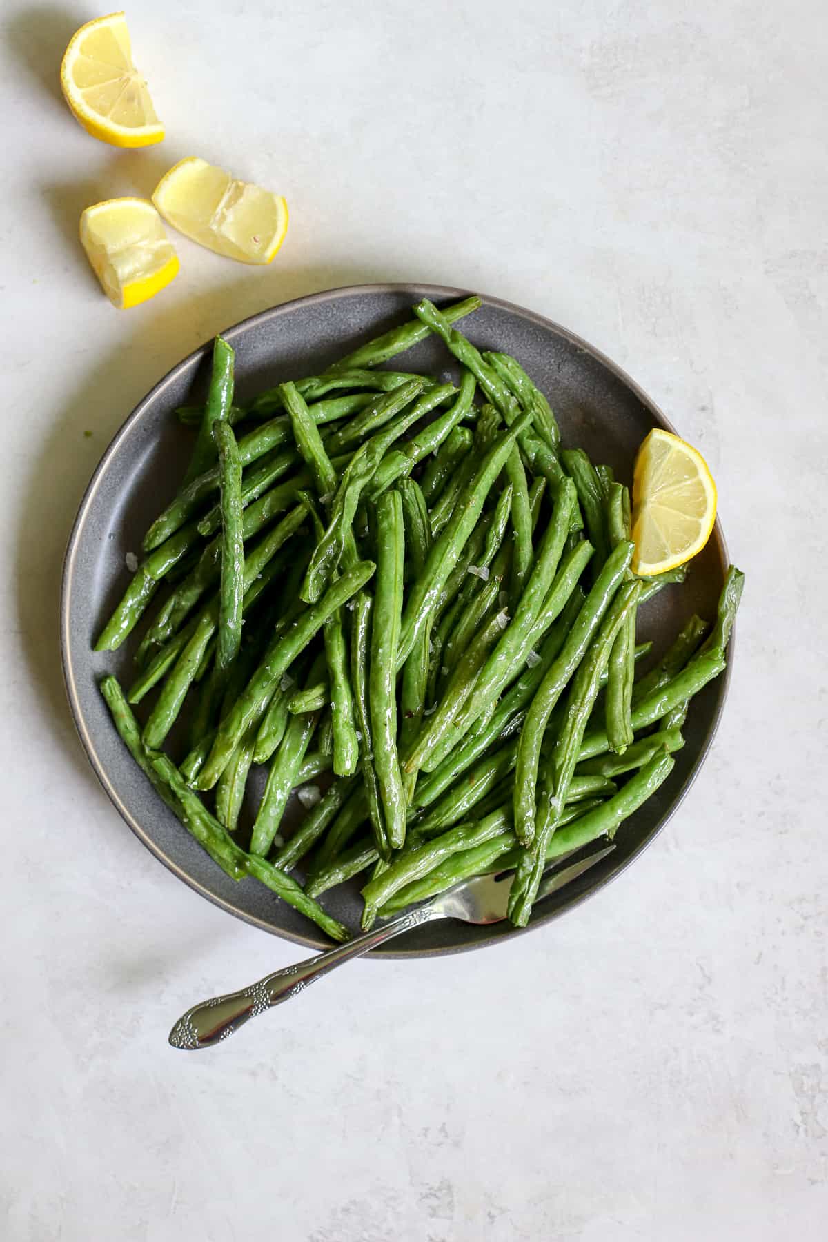 Air fryer green beans on gray plate with lemon wedges, on gray and white surface